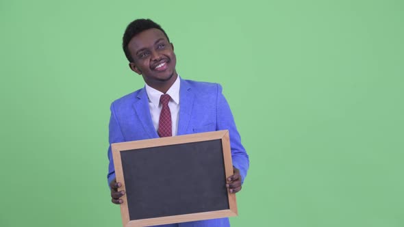 Happy Young African Businessman Thinking While Holding Blackboard