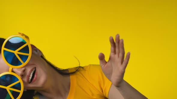 Woman in Funny Yellow Hippie Sunglasses is Fooling Around on a Yellow Background