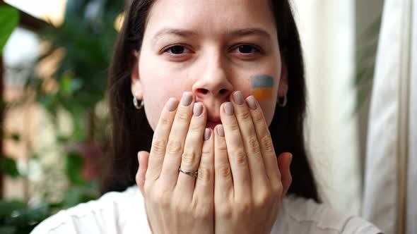 Young Sad Ukrainian Girl with the Flag of Ukraine and Russia on Her Face is Opening Her Eyes