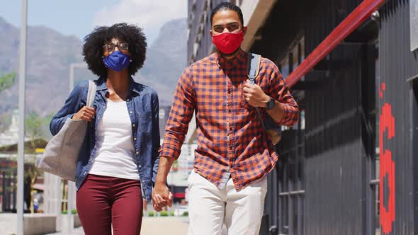 Diverse couple wearing face masks walking and holding hands