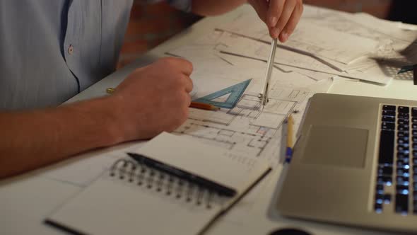 Hands of Caucasian Male in Blue Shirt Making Measurements on Drawing with Dividers and Making Notes