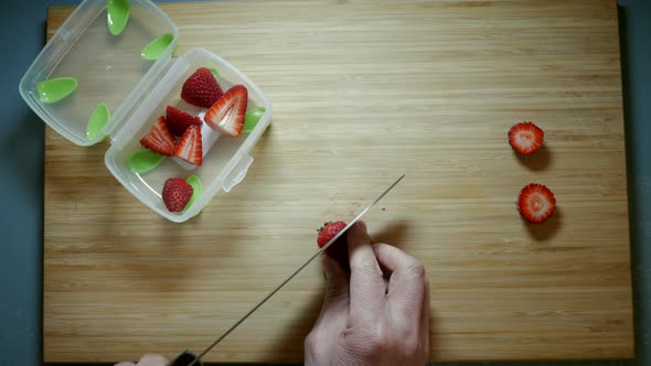 Strawberries being sliced on a bamboo chopping board. Fruit being prepared for children’s lunch. Top