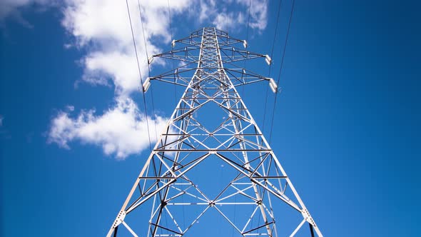 Looking up at electric pylon as clouds pass in blue sky, timelapse