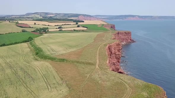 STATIC CROP, Slow pan across green seaside fields by red sandstone cliffs