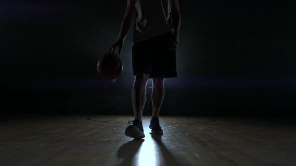 Basketball Player in Sportswear Red Shorts and a Blue T-shirt Goes on a Dark Basketball Court in the