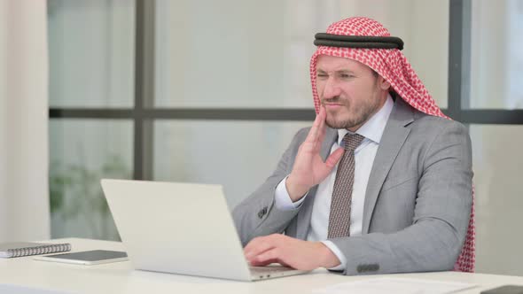 Middle Aged Arab Businessman having Toothache while using Laptop in Office