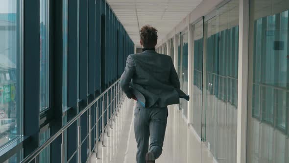 Young businessman running along long office corridor with window corridor back view of camera. Man i