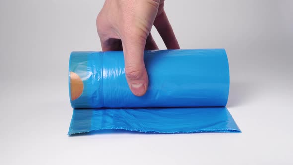 A hand picks up a new roll of blue trash bags from a white surface