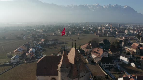 Aerial of Swiss flag flying on top of castle tower. Drone pulling back and revealing the beautiful,