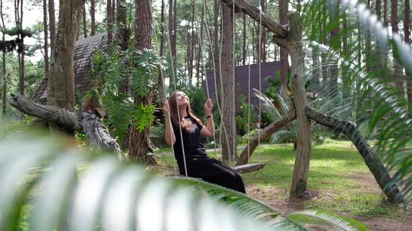 A young asian woman sitting on a wooden swing and looking at a beautiful green nature