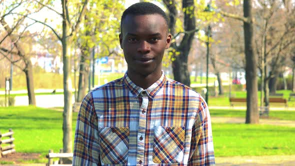 A Young Black Man Smiles at the Camera in a Park on a Sunny Day