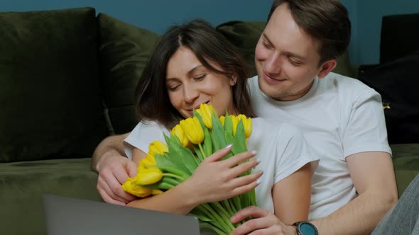 Woman That Is Working at the Computer Receiving a Bouquet of Yellow Tulips From Her Husband