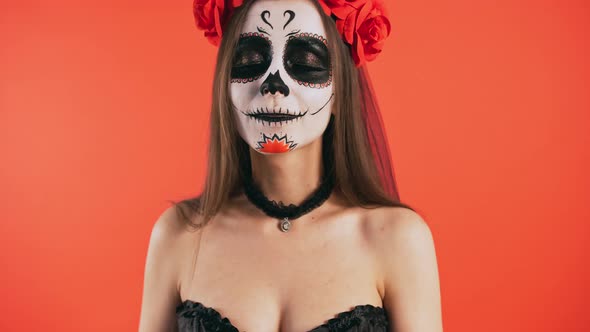 Day of Dead Woman with Sugar Skull Makeup Smiling and Sending you an Air Kiss Posing on Red