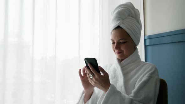 Close-up Portrait of Woman in Bathrobe, with Towel on Her Head, Uses Mobile Phone