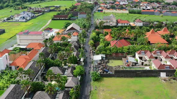 scooters and car traffic driving on road near tropical rice fields in Berawa Bali, aerial