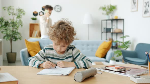 Little Boy Writing Studying Doing Homework While Mother Talking on Mobile Phone at Home