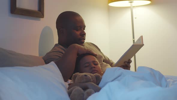 Afro-American Dad Reading Book to Sleeping Kid in Bedroom