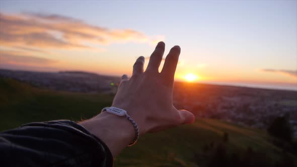 Hand of a man reaching for the sun at sunset.