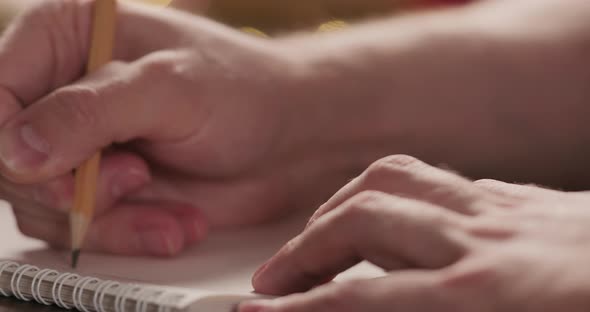 Closeup Man Writes Christmas Gifts Notepad Pencil Under Warm Light Evening