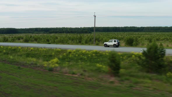 Aerial View of a Car Driving Along the Road Among Fields of Green Grass