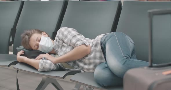 Tired Young Caucasian Woman in Face Mask Sleeping on Chairs in Waiting Area of Airport, Bus or