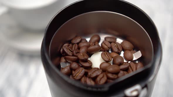 Fills the grinder with roasted coffee beans with a spoon.