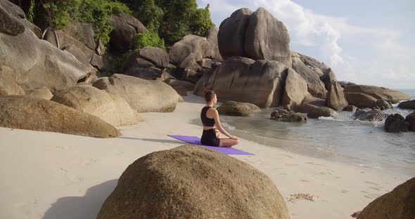 Sport Woman Meditating at Exotic Beach, She Seats on Beach Line Near the Water
