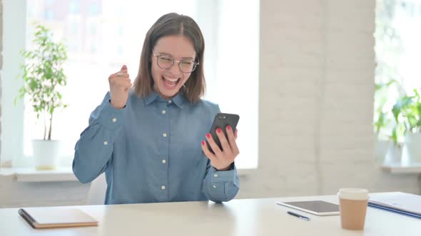 Young Woman Celebrating Success on Smartphone in Office