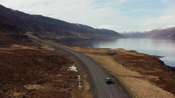 Drone Tracking Car Driving By Fjord And Towards Mountains