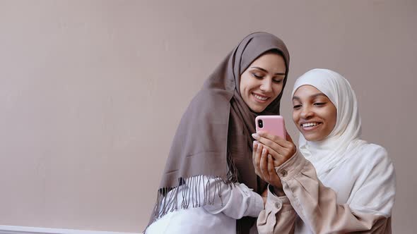 Two Muslim Girl Look at the Phone Smiling and Laughing