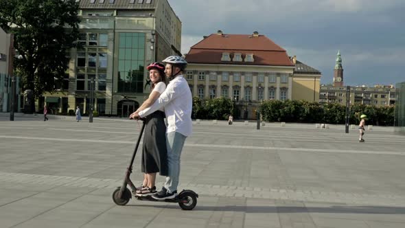 Young Man Rides His Girlfriend on an Electric Scooter in the City Square