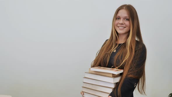 A Schoolgirl in a Good Mood with a Pile of Books alt