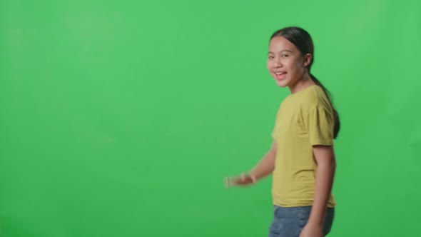 The Happy Young Asian Kid Girl Walking And Waving Hand Say Bye Bye While Standing On Green Screen