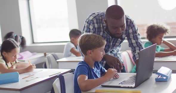 Video of happy african american male teacher helping caucasian boy with laptop