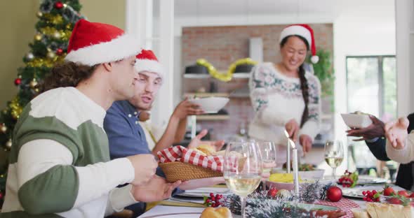 Happy group of diverse friends in santa hats celebrating meal at christmas time