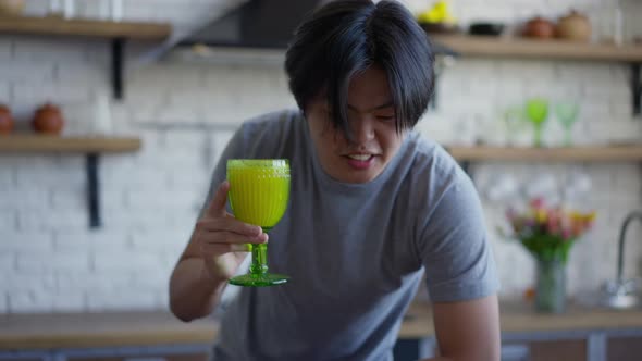 Zoom Out From Cheerful Asian Young Man Holding Glass of Healthy Smoothie Talking Looking at Tablet