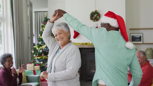 Happy diverse senior couple dancing together with friends in background at christmas time