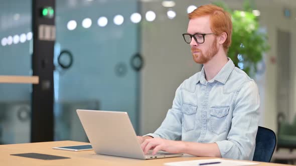 Sick Young Redhead Man with Laptop Coughing in Office