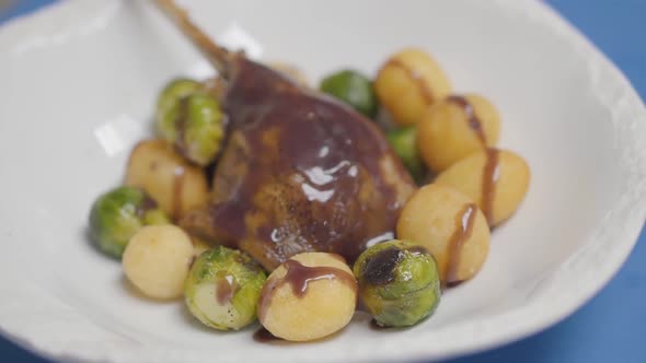 White Plate with Duck Leg, Potato Balls and Brussels Sprouts on the Sause Close Up