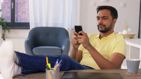 Indian Man with Smartphone Resting Feet on Table