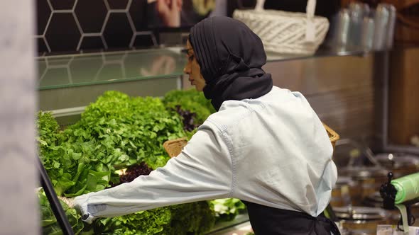 Woman in Scarf Refill the Fresh Greens on the Shelf at the Supermarket