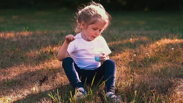 Young Lady Eats Yogurt with Metal Spoon Sitting on Meadow