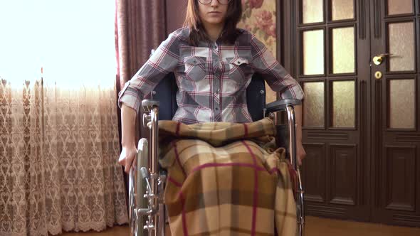 Young Woman on a Wheelchair. The Girl Moves in a Wheelchair Around the House. The Girl Is