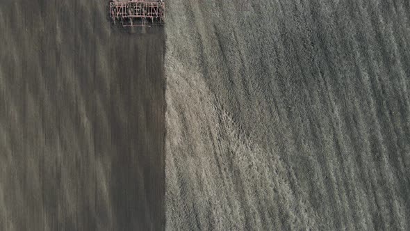 Aerial view of a modern yellow tractor plowing dry agricultural field , preparing land for sowing