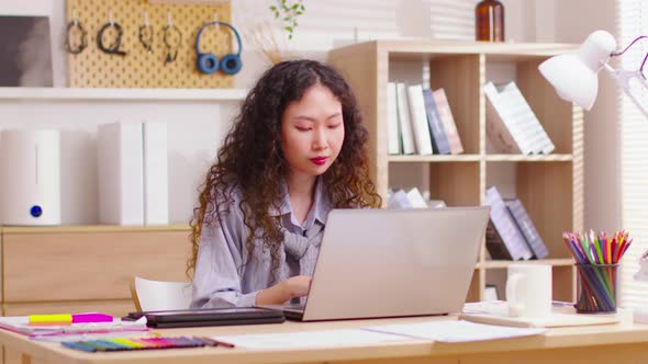 Energetic Asian businesswoman working on laptop from home office. Using computer remote studying, br