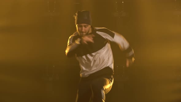 Young Man in Tracksuit Dancing Breakdance Street Dance in a Smoky Yellow Backlit Studio. Close Up.