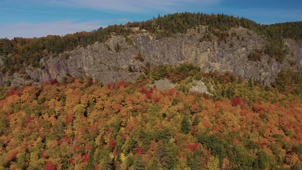 Aerial slide to the right along the cliff face of Kineo Mountain above a golden autumn forest