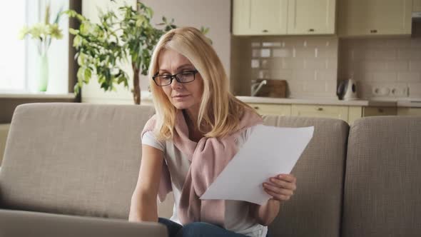 Mature Woman Sitting at Her Desk with Paper Letter Document and Laptop