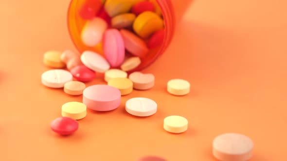 Close Up of Many Colorful Pills and Capsules Spilling on Orange Background