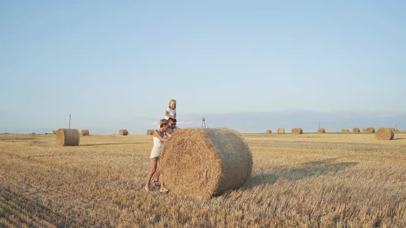 Happy Family with Little Daughter Rolling a Haystack in Sunny Field